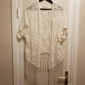 Vit spetskofta från Hollister strl M - Säljer en vacker vit spetskofta från Hollister. Koftan har korta ärmar och fransar längs nederkanten, vilket ger en bohemisk känsla. Perfekt för att lägga till en romantisk touch till din outfit. 🕊️