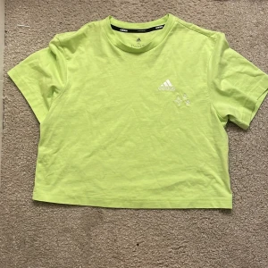 Limegrön t-shirt från Adidas - Säljer en fräsch limegrön t-shirt från Adidas. Den har en kortärmad design och är tillverkad i ett mjukt bomullsmaterial. Perfekt för en sportig look eller avslappnad stil. Adidas-loggan är tryckt i vitt på bröstet. Passar perfekt för varma dagar eller träning. testat en gång men hade jag använt