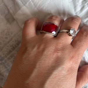 Ring med stor röd sten - Elegant ring med en stor, fyrkantig röd sten infattad i en silverfärgad ram. Perfekt för att ge en färgklick till din outfit.