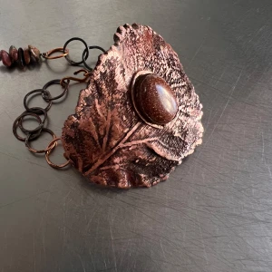 Handgjort armband med kopparlöv och sten - Unikt armband med ett stort lövformat hänge i koppar och en brun skimrande sten i mitten. Kedjan består av stora ringar i koppar och dekoreras med små färgade stenar. Perfekt för dig som gillar naturinspirerade smycken.