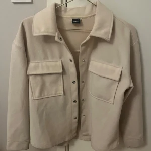Beige jacka - Säljer en beige lite tunnare jacka med stora bröstfickor och tryckknappar framtill. Skjortan har klassisk krage och långa ärmar, perfekt att styla lager på lager. Enkel och stilren design som passar till mycket.🩷