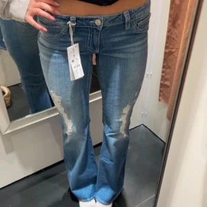 Blå bootcut jeans med slitningar - Säljer ett par Lågmidjade blå bootcut jeans med slitningar framtill och snygga detaljerade bakfickor. Jeansen har snygg passform och klassisk femficksdesign. Från Gina Young 14+ i storleken M men upplever att den sitter mer som en vanlig S💕💕endast använda vid ett fåtal tillfällen 