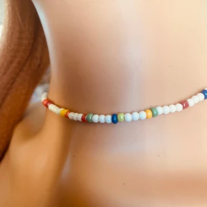By prisförslag- Färgglatt vitt pärlhalsband  - Snyggt och färgglatt halsband med små pärlor i olika färger som vitt, rött, blått, gult och grönt. Perfekt för att ge en färgklick till din outfit.