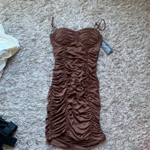 Brun tight klänning från Boohoo - Snygg brun klänning från Boohoo med rynkade detaljer och smala axelband. Perfekt för en utekväll. Klänningen har en tight passform. Aldrig använd, prislapp sitter på. Kan gå ner i pris vid snabb affär.💖