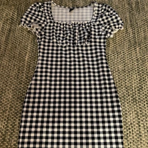 Svartvit rutig klänning från Shein - Säljer en svartvit rutig klänning från Shein med korta ärmar och volangdetaljer vid halsen. Den är köpt på SHEIN i storlek S