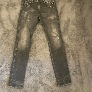 Gråa Replay Anbass - Snygga grå jeans från Replay, modell Anbass. De har en slim passform med slitna detaljer. Högt eftertraktade och säljs ej i butik längre. Perfekta för en avslappnad stil. Storlek 30/34 
