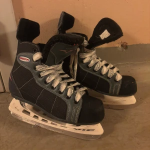 Svarta skridskor från Roxon - Säljer ett par svarta skridskor från Roxon med vita snören och robust design. Perfekta för vinterns isäventyr. De har en klassisk look med vadderad ankel för extra komfort.