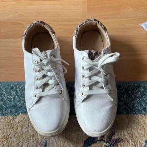 Vita sneakers med leopardmönster - Snygga vita sneakers med snörning och leopardmönstrad insida. Perfekta för en stilren look med en touch av djurmönster. Bekväma och lätta att matcha med olika outfits.  storlek 38 använda men bra skick.