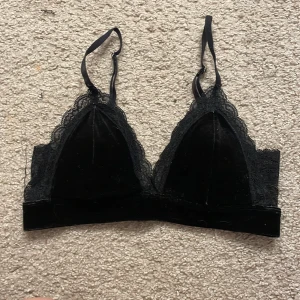 Svart spetsdetaljerad bralette från Lindex - Snygg svart bralette från Lindex med spetsdetaljer och justerbara axelband. Perfekt för en stilren look med en touch av elegans. Den har en mjuk och bekväm passform med hakknäppning bak.