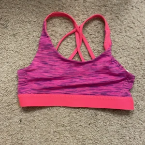 Rosa sporttopp från H&M - Säljer en rosa sporttopp från H&M med korsade axelband och ett mönster i mörkare rosa nyanser. Perfekt för träning med sin bekväma passform och elastiska material.