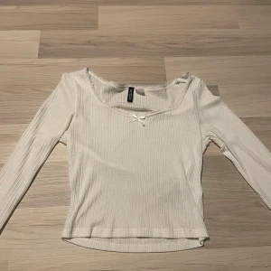 Vit ribbad topp  - Säljer en söt vit ribbad topp från H&M med en liten rosett framtill. Toppen har långa ärmar och en fin fyrkantig halsringning.