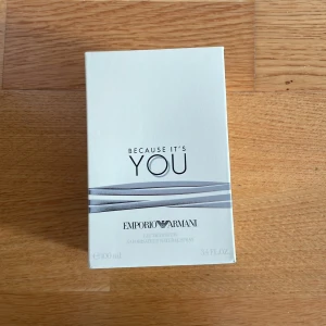 Because It's You Eau de Parfum från Emporio Armani - Säljer en elegant parfymflaska av Emporio Armani, 'Because It's You'. Flaskan är genomskinlig med en silverfärgad kork och rymmer 100 ml av en varm, bärnstensfärgad doft. Förpackningen är stilren och vit med subtila grå detaljer. Perfekt för den som vill ha en sofistikerad och modern doft.