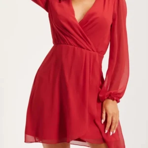 Röd omlottklänning - Snygg röd omlottklänning med långa ärmar och v-ringning. Perfekt för en kväll ute eller en speciell tillställning. Klänningen har en elegant passform och är tillverkad i ett lätt och luftigt material.