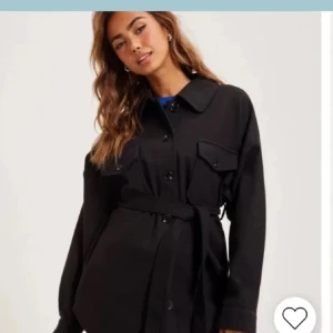 Svart kappa med bälte - Snygg svart kappa från Nelly med knappar och bälte i midjan. Perfekt för en stilren look. Nästan helt oanvänd.