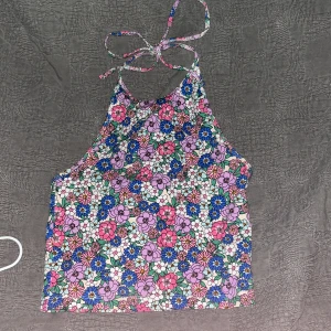 Blommig knyt topp - Säljer en färgglad halterneck-topp med blommigt mönster i rosa, blått och vitt. Toppen har en knytning i nacken och är perfekt för sommarens varma dagar.