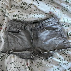 Grå jeansshorts med fransar - Säljer ett par grå jeansshorts med fransiga kanter. Shortsen har en klassisk femficksdesign och knappgylf. Perfekta för en avslappnad sommarlook.