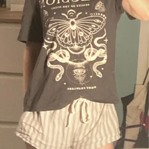 Aestetisk pyjamastopp - Säljer en svart t-shirt med ett coolt tryck av en fjäril och ormar. T-shirten har korta ärmar och en avslappnad passform. Perfekt för en casual look!