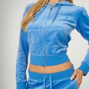 Blå juicy couture kofta med dragkedja - Snygg blå velour kofta från juicy couture med dragkedja och huva. Jackan har långa ärmar och en broderad logga på bröstet. Perfekt för en avslappnad stil. Nypris:1000kr, den är använd fåtal gånger 
