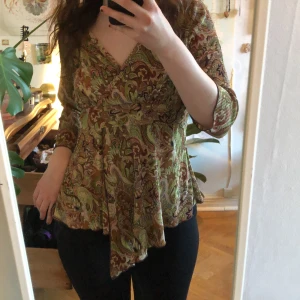 Mönstrad topp i gröna och bruna toner - Säljer en snygg topp med ett livfullt mönster i gröna och bruna nyanser. Toppen har trekvartsärmar och en v-ringad design som ger en elegant touch. Perfekt för att ha på en hippiefest ☺️