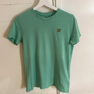 Grön t-shirt från Lyle & Scott - Säljer en snygg grön t-shirt från Lyle & Scott i storlek 12/13 år. T-shirten är tillverkad i 100% bomull och har en liten broderad logga på bröstet. Perfekt för en avslappnad stil! Hör av er vid frågor :)