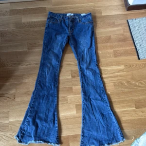 Blå bootcut jeans från AC FOR AG - Snygga blå bootcut jeans från AC FOR AG med fransade kanter. Perfekta för en avslappnad stil med en touch av retro. De har en klassisk femficksdesign och är tillverkade i ett bekvämt denimtyg.
