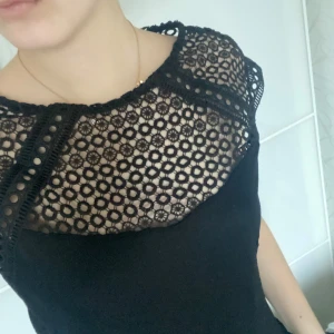 Svart topp med spetsdetaljer från H&M - Snygg svart topp från H&M med vackra spetsdetaljer upptill. Toppen har en elegant design med korta ärmar och en normal passform. Perfekt för att ge en stilren touch till din outfit.