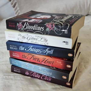 Bloodlines-serien av Richelle Mead - Säljer en komplett samling av Bloodlines-serien av Richelle Mead. Böckerna inkluderar 'Bloodlines', 'The Golden Lily', 'The Indigo Spell', 'The Fiery Heart', 'Silver Shadows' och 'The Ruby Circle'. Perfekt för fans av vampyrromaner och fantasy. Böckerna har vackra omslag med porträtt och dekorativa element.