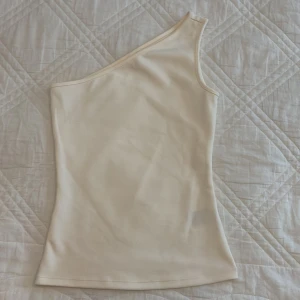 Beige oneshoulder topp - Snygg beige oneshoulder topp som ger en stilren look. Perfekt för att skapa en trendig outfit. Toppen är aldrig använt säljer för att den är för liten 