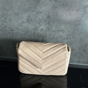 Beige quiltad axelväska med kedja - Snygg beige axelväska med quiltat mönster och guldfärgad kedja. Perfekt för att ge en stilren touch till din outfit. Väskan har en praktisk storlek och en elegant design. skriv till mig om du är intresserad eller har några frågor 🥰