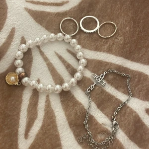Smyckeset med pärlarmband och silverringar - Elegant smyckeset med ett pärlarmband dekorerat med ett guldigt snäckskalshänge och tre stilrena silverringar. Även ett silver armband(inte äkta) har använt allt en gång 