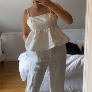 Vit ärmlös topp med volang - Säljer en söt vit ärmlös topp med volangdetaljer. Toppen har smala axelband och en luftig passform.  Den är storlek s men passar både xs och m, då man knyter hur man vill att den ska sitta och man kan reglera axelbanden. Från Gina tricot premium kollektion 