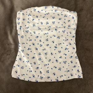 Vit blommig tubtopp - Säljer en söt vit tubtopp med blå blommor. Perfekt för sommardagar och kan enkelt matchas med jeans eller kjol. Aldrig använd och har därför tyvärr inga bilder med den på, men hör av dig om du har funderingar!💕