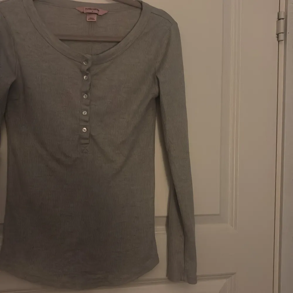 Säljer en grå långärmad tröja från Hunkemöller. Tröjan har en knappdetalj framtill och är perfekt tröja att sova i. Den är tillverkad i ett mjukt material som känns skönt. . T-paidat.