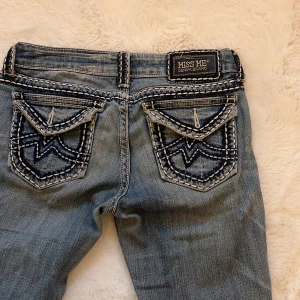 Blå bootcut jeans från Miss Me - Snygga blå bootcut jeans från Miss Me med dekorativa bakfickor och slitningar. Jeansen har en låg midja och coola detaljer som ger en unik look. Perfekta för en avslappnad stil.