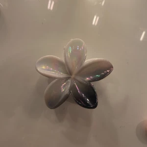 Vit hårklämma i form av en blomma - Snygg vit hårklämma formad som en blomma med en glansig yta. Perfekt för att sätta upp håret med stil.