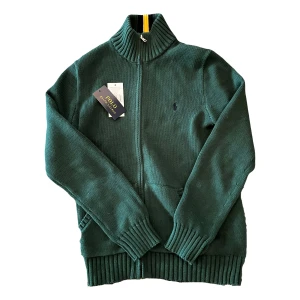 Grön stickad tröja från Polo Ralph Lauren - Säljer en snygg grön stickad tröja från Polo Ralph Lauren med dragkedja | säljs pga inte används och för liten |helt ny | ny pris:1595 | vårt pris: 1395 | tags finns | pris är inte hugget i sten 🪨 |