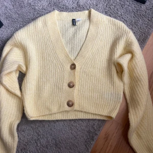 Gul stickad kofta från H&M - Säljer en söt gul stickad kofta från H&M:s Divided-kollektion. Koftan är croppad med en v-ringning och har tre knappar framtill. Aldrig använt💛