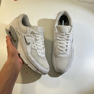  Nike Air Max 90 - Säljer ett par stilrena vita Nike Air Max 90 jewels med synlig luftdämpning i sulan. Skorna har snörning och en rund tå, vilket ger en klassisk look. Perfekta skor nu till sommaren, kvitto finns.