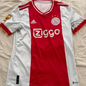 Röd och vit Ajax fotbollströja från Adidas - Säljer en snygg Ajax fotbollströja från Adidas i rött och vitt. Tröjan är i bra skick och inga problem med den. 