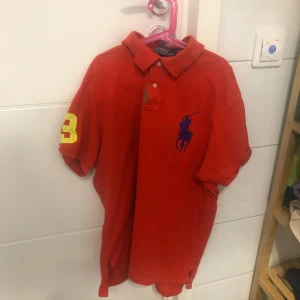 Röd pikétröja från Ralph Lauren - Säljer en röd pike som är i bra skick. Dock har den små märken två vid bröstet och en på ryggen, som knappt går att se