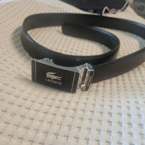 Svart bälte från Lacoste - Snyggt svart skärp från Lacoste med en stilren silverfärgad spänne. 