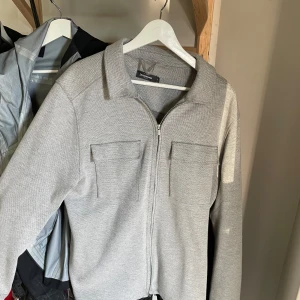 Grå cardigan jacka med dragkedja - Säljer en stilren grå cardigan jacka med dragkedja och två bröstfickor. Perfekt för en avslappnad look. Jackan har långa ärmar och en klassisk krage.  andvänd ca 2 gånger ingen söm är trasig eller nåt pris kan diskuteras