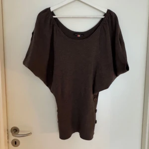 Brun tröja från Louise Orop - Säljer en brun tröja från Louise Orop med korta ärmar och knappar på sidan. Tröjan har en rund halsringning och ribbad nederkant. Perfekt för en avslappnad stil. Vääääärldens bästa fest topp