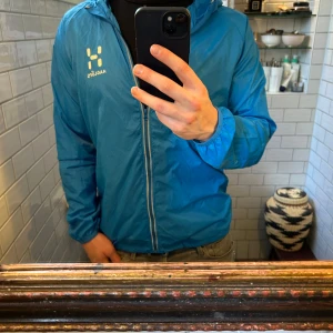 Blå windbreaker från Haglöfs - Säljer en blå vindjacka från Haglöfs med dragkedja framtill. Jackan har långa ärmar och en praktisk huva. Perfekt nu till våren, väldigt stilren! Pm vid funderingar!