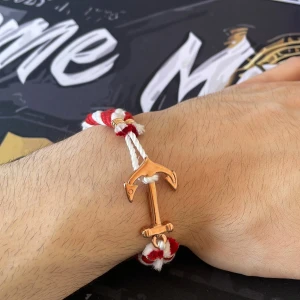 armband - Snyggt armband med tvinnat band i rött och vitt och ett ankare i guldfärgad metall som lås. Perfekt accessoar för en nautisk vibe och passar till både chill och statement outfits. Bandet är grovt tvinnat och ankaret ger en cool detalj.