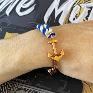 Armband - Snyggt armband med guldigt ankare som lås, kombinerat med flätad brun rem och tvinnade band i blått och vitt. Perfekt accessoar för en cool och avslappnad stil med marina vibbar.