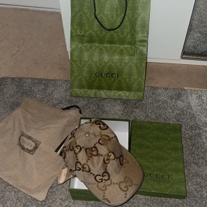 Gucci keps  - Snygg beige keps från Gucci med det klassiska GG-monogrammet i brunt över hela kepsen. Kepsen har böjd skärm och är tillverkad i ett slitstarkt canvasmaterial. Kommer med originalpåse och låda för extra lyxig känsla.