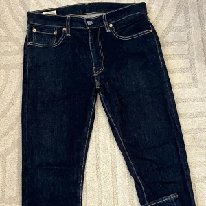 Levi's Premium Skinny Taper jeans blå - Snygga Levi's Premium jeans i mörkblå denim med skinny taper passform. Klassiska femficksdetaljer, kontrastsömmar och läderpatch bak. Perfekta för dig som gillar en smalare siluett och stilren look.