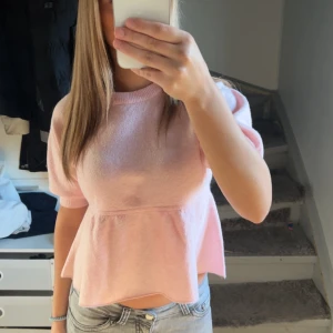 Ljusrosa peplum topp med kort ärm - Supersöt ljusrosa topp med peplumskärning och korta puffärmar. Mjuk och skön, perfekt till jeans eller kjol. Rund halsringning och avslappnad passform ger en gullig och trendig look.