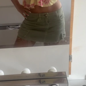 Olivgrön jeanskjol med fickor - Säljer en olivgrön kort jeanskjol med råa kanter och stora sidfickor. Kjolen har klassisk knapp och dragkedja framtill samt bälteshällor. Perfekt för dig som gillar en chill och trendig stil., uppklipt ifrån hina tricot, inga defekter